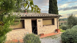 Une maison de campagne en pierre, avec un toit en tuiles, une cheminée et un petit jardin agrémenté de chemins de gravier et de diverses plantes.