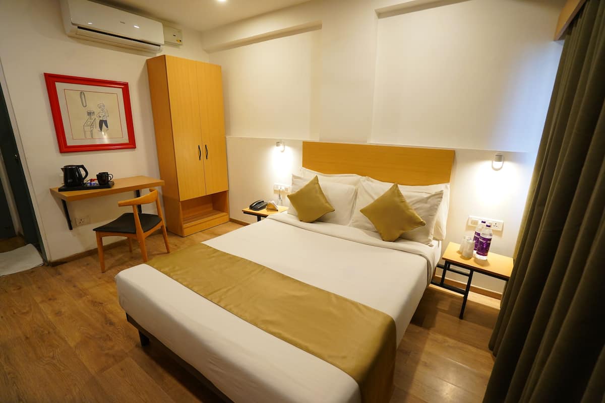 A hotel room with a bed, a desk, a chair, a wardrobe, a bedside table with a lamp, and a picture on the wall.
