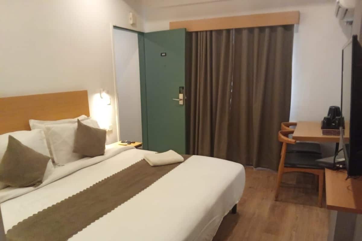 A hotel room with a bed, a desk, a chair, a television, and a door.