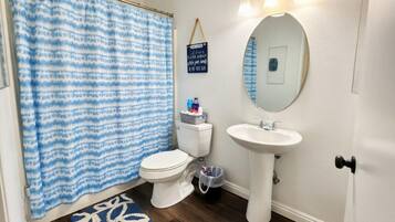 A bathroom with a white toilet, a white sink, a blue and white shower curtain, and a small rug.