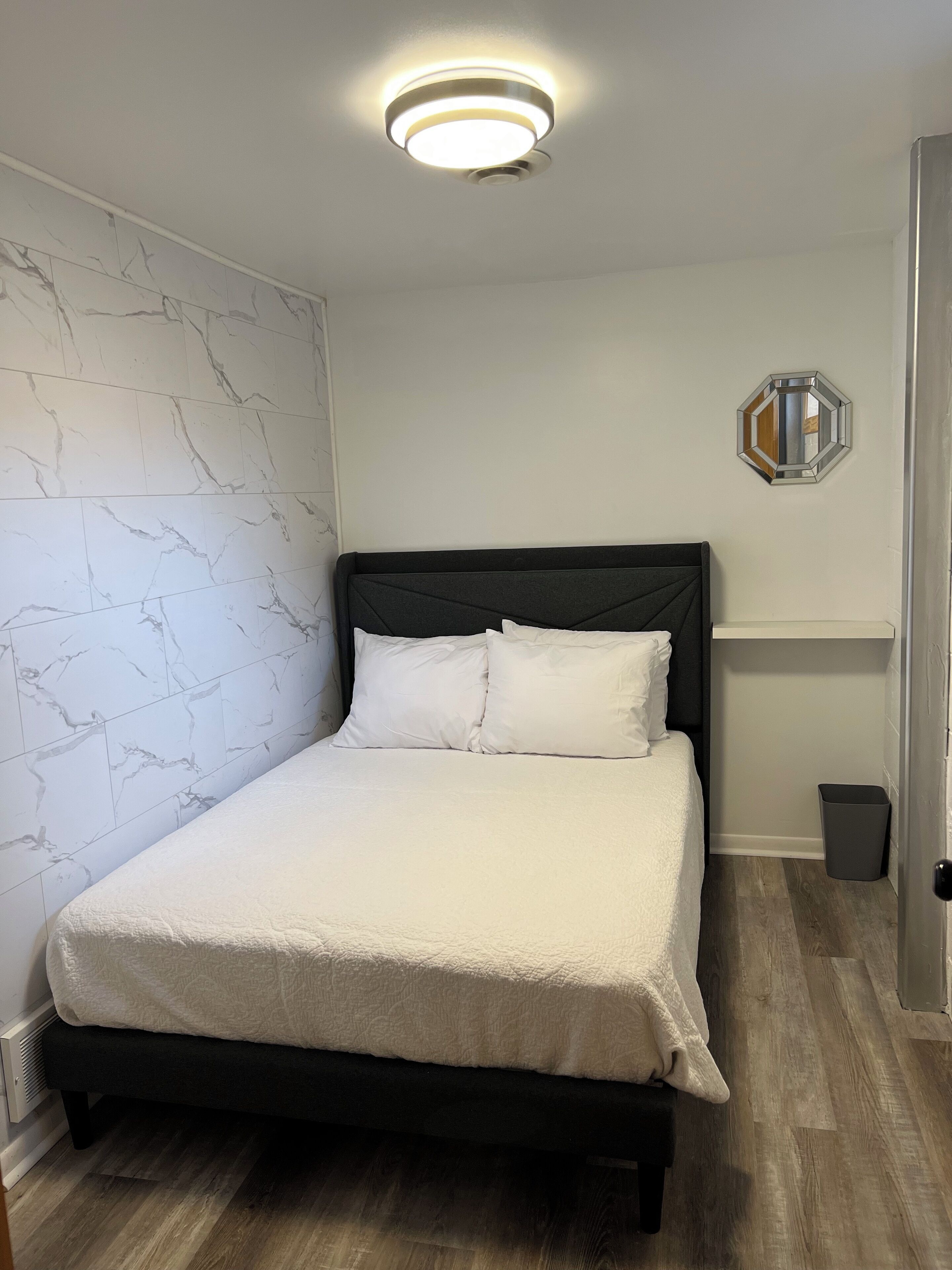 Een net opgemaakt bed met een donker hoofdbord en witte beddengoed in een kamer met wanden in marmerlook en een houten vloer.