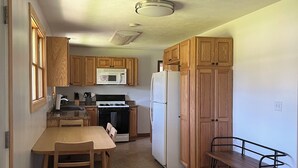 A kitchen with wooden cabinets, a microwave, stove, refrigerator, and a dining area with a bench. - M-28 House
Direct Trail Access - Ample Trailer Parking - Year-Round Fun (Marquette)