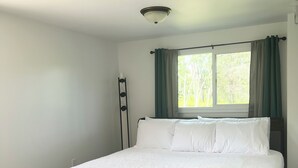 A bedroom with a large bed, a window with curtains, and a ceiling light fixture. - M-28 House
Direct Trail Access - Ample Trailer Parking - Year-Round Fun (Marquette)