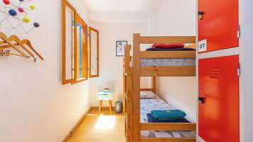 Quarto com beliche, escada de madeira, pequena escrivaninha com cadeira, lixeira e armário vermelho identificado com o número 07.