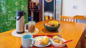 Una mesa de desayuno con una cafetera, un bol de fruta, un plato con un sándwich, una taza y un bol de cereal.