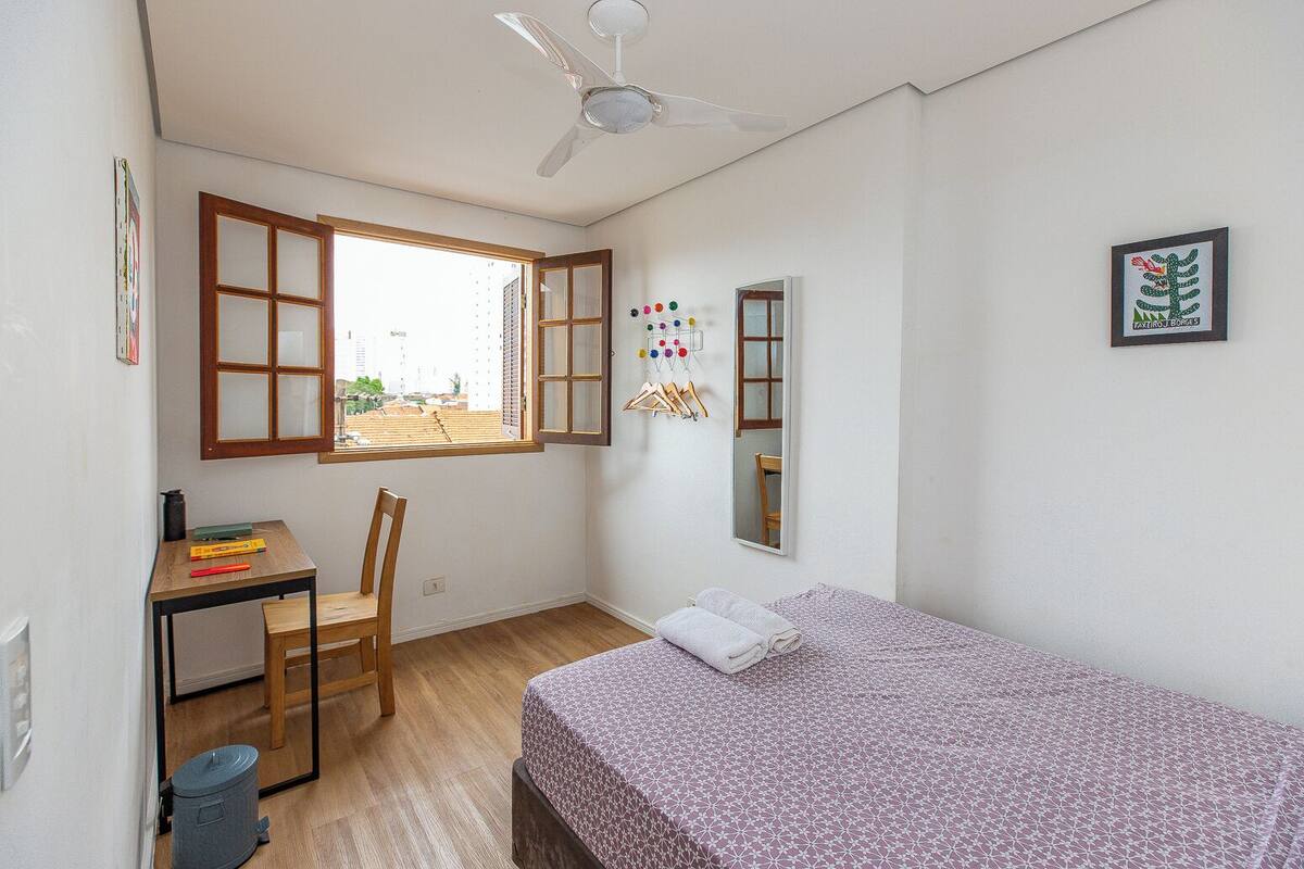 A small, clean room with a bed, a desk, a chair, and a window.