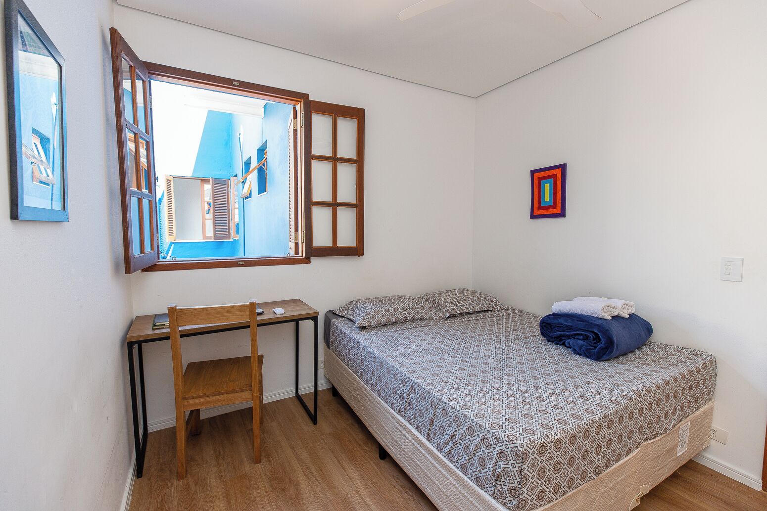 A small, neatly arranged bedroom with a single bed, a desk, and a chair.
