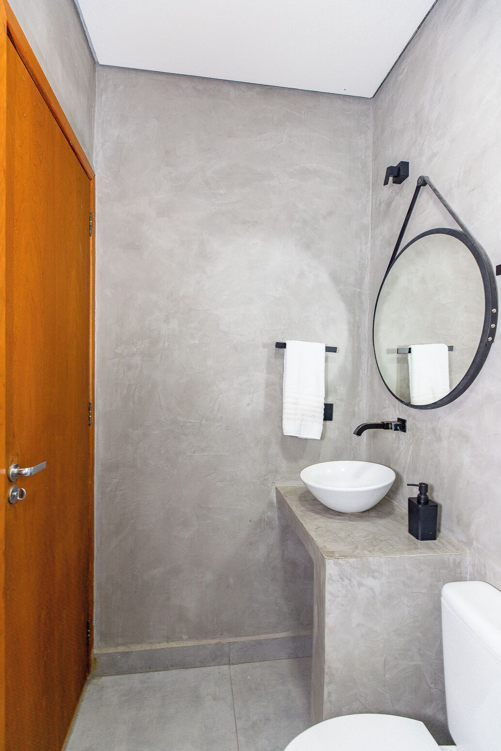 A bathroom with a wooden door, a white sink, a round mirror, and a towel rack.