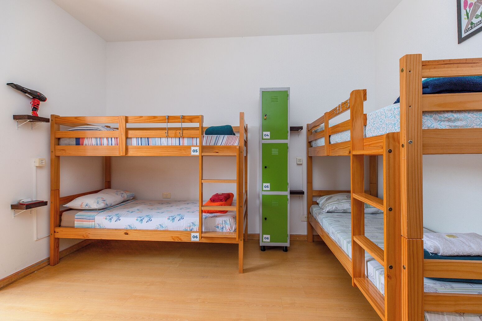 Um quarto tipo dormitório com beliches, um móvel de armazenamento verde e uma estante com livros e um objeto vermelho.