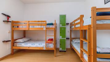 Um quarto tipo dormitório com beliches, um móvel de armazenamento verde e uma estante com livros e um objeto vermelho.