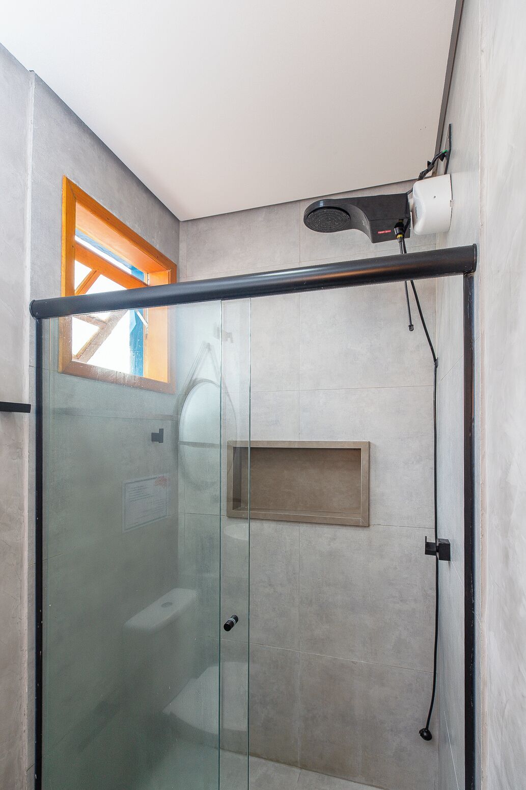 A modern bathroom with a glass shower enclosure, a built-in shelf, and a hairdryer mounted on the wall.