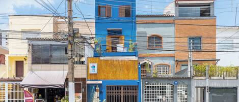 Un immeuble à plusieurs étages, doté d’une façade bleue, d’une section recouverte de panneaux en bois et d’une entrée fermée par un portail.