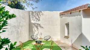 A patio with a table and chairs, a small window, and a concrete wall. - La Suite Soleil - Maison studio avec jardin privé (Décines-Charpieu)