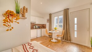 A modern apartment with a kitchen, dining area, and a large window. - La Suite Soleil - Maison studio avec jardin privé (Décines-Charpieu)