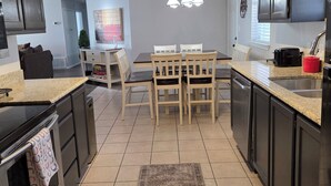 A modern kitchen with dark cabinets, a granite countertop, a central island, and a dining area with a chandelier. - Rustic Wheel-horse House. Entire one-level 3/2 home located in Granbury, TX. (Granbury)