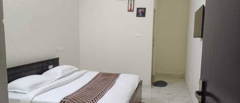 Un dormitorio con una cama, un televisor de pared y una puerta.