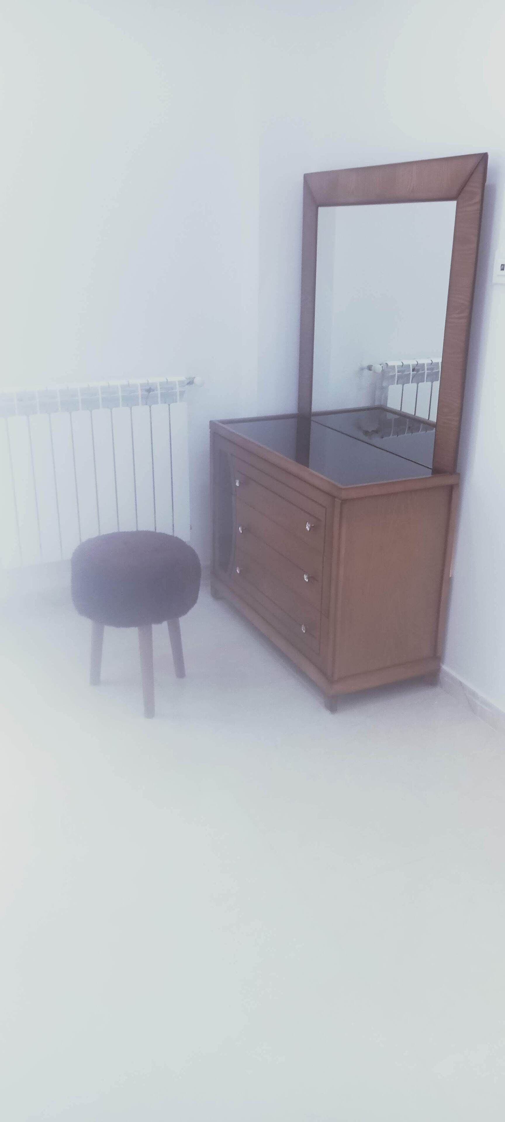 Et hjørneværelse med en trækommode, en lille skammel og en radiator.