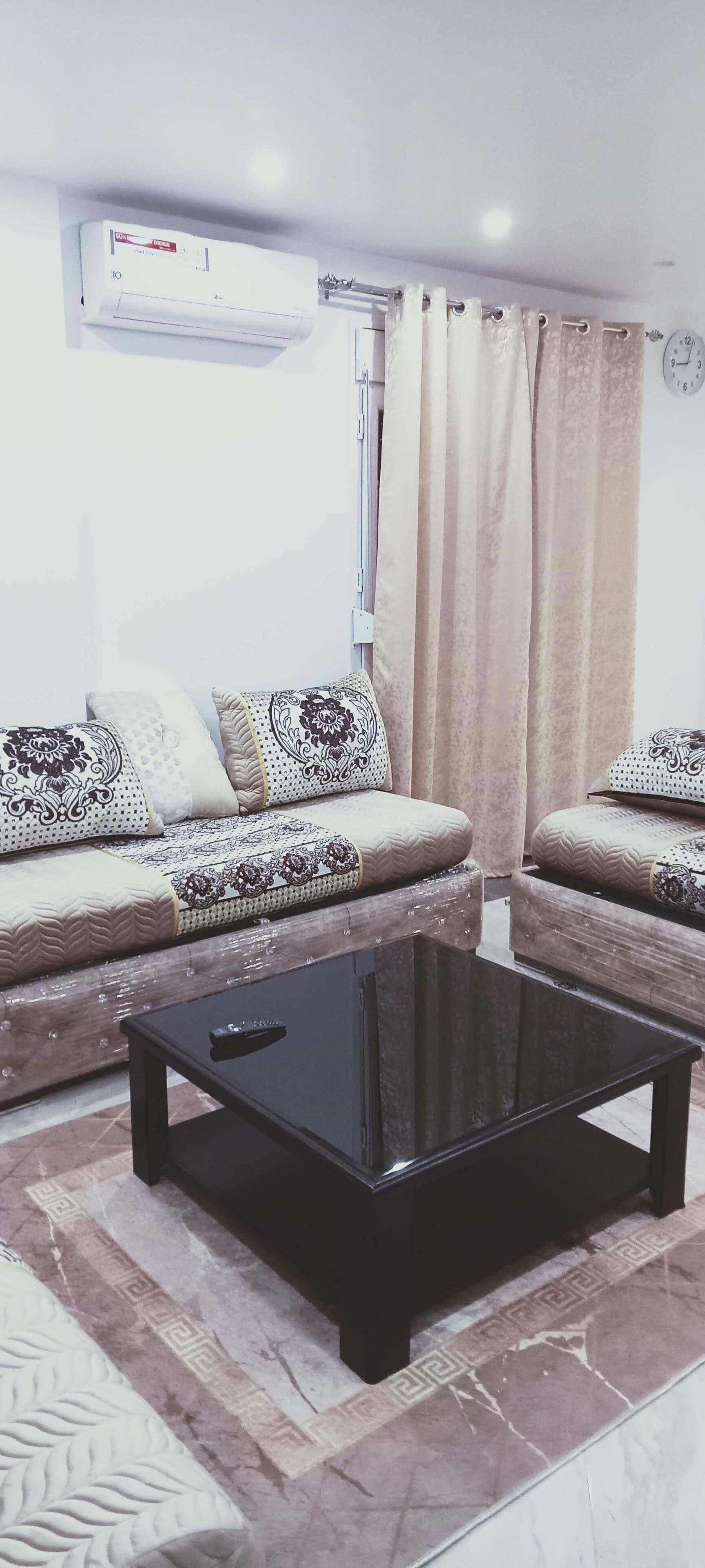 Un salon avec deux canapés, une table basse noire, des coussins à motifs, une horloge et un appareil de climatisation.