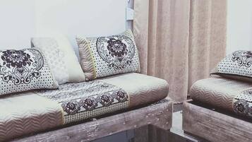 Un salon avec deux canapés, une table basse noire, des coussins à motifs, une horloge et un appareil de climatisation.