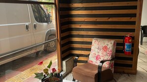 Esquina de una habitación con un muro de listones de madera, un sillón floral, una mesa blanca y una planta en maceta.