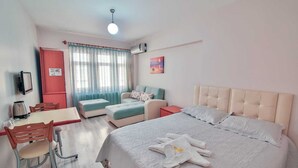 Habitación de hotel con cama, escritorio con silla, una mesita, un armario rojo y ventana con cortinas.