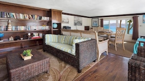 Una sala de estar acogedora con sofá, estantería, comedor y vista al mar.