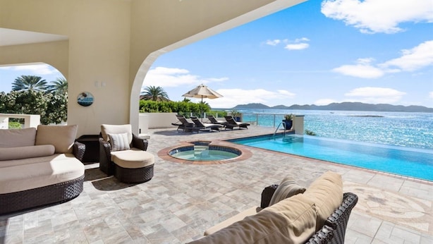 Zona de piscina con sillones de descanso y un jacuzzi, con vista a un mar azul cristalino y montañas lejanas.
