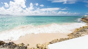 Una playa con aguas turquesas cristalinas, arena blanca y afloramientos rocosos.
