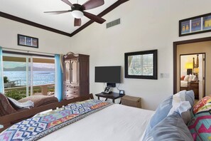A hotel room with a bed, a TV, a desk, a wardrobe, and a balcony with a view of the sea. - Dolphin at Anguillitta: 3BR Beachfront, Book Now! (Blowing Point)