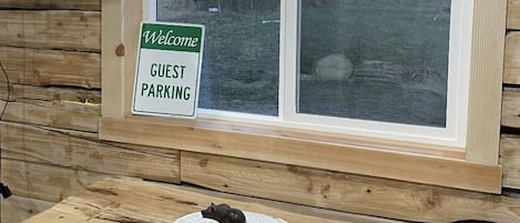 A wooden cabin interior with a sign indicating guest parking, a television mounted on the wall, and a view of snow-capped mountains through a window.
