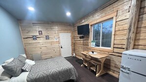 Una habitación pequeña con cama, un escritorio, televisor y refrigerador.