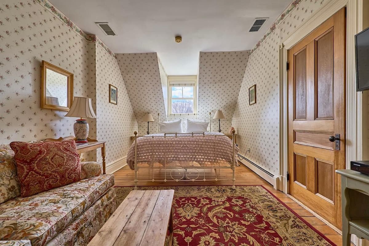 Un dormitorio con cama, sofá, banco de madera, ventana y puerta.