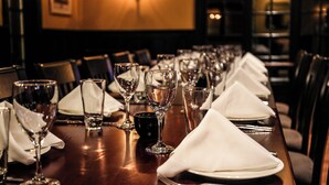 Una larga mesa de comedor dispuesta con varios vasos de vino, vasos de agua y servilletas blancas dobladas.