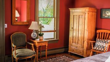 Une pièce comprenant une chaise en bois, un meuble en bois, une table avec une lampe et une fenêtre avec des stores.