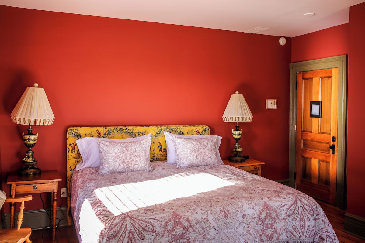 Una habitación con una cama, dos lámparas de noche, una puerta de madera y una mesita.