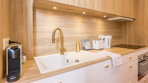 A modern kitchen with a wooden backsplash, a gold faucet, a coffee maker, and a Krups electric kettle.
