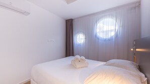 Ein Hotelzimmer mit einem ordentlich bezogenen Bett, einem großen Fenster mit Vorhängen und einer wandmontierten Klimaanlage.