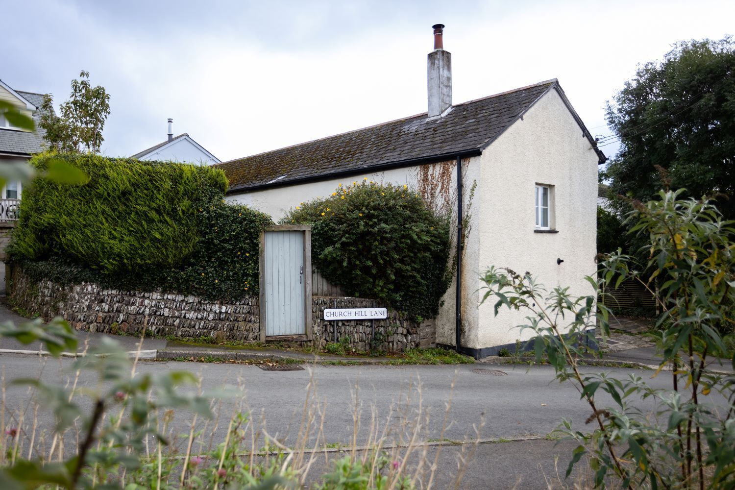 A small white building with a stone wall and a wooden door, labeled "Church Hill Lane."