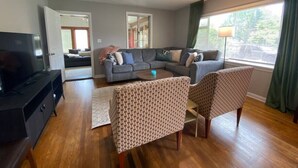 Een moderne woonkamer met een hoekbank, twee fauteuils met dessin, een salontafel en een televisie op een zwart dressoir.