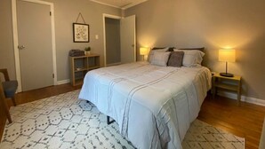 Een slaapkamer met een groot bed, een plafondventilator, een nachtkastje met lamp en een deur naar een andere kamer.