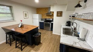 Cocina compacta con una isla de madera, horno integrado y lavamanos con encimera de mármol.