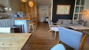 Une cuisine moderne avec des meubles en bois, un coin repas avec des chaises bleues et un salon avec un canapé et une carte accrochée au mur.