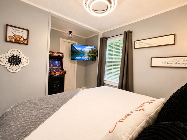 Een slaapkamer met een bed, een televisie, een wandklok en een deur naar een andere kamer.
