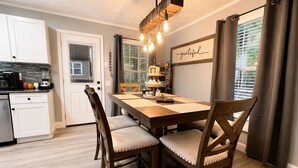 A dining area with a wooden table, cushioned chairs, a chandelier, and a wall with a 'grateful' sign. - Dollywood Cabin - Luxury with Private Arcades (Sevier County)