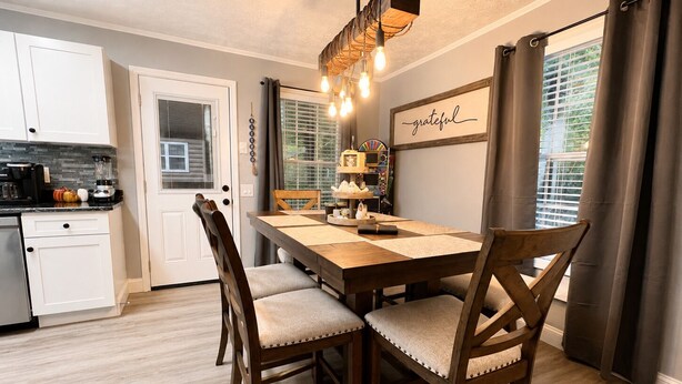 A dining area with a wooden table, cushioned chairs, a chandelier, and a wall with a 'grateful' sign.
