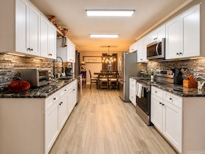 A modern kitchen with white cabinets, a microwave, a refrigerator, and a dining area with a chandelier.