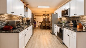 A modern kitchen with white cabinets, a microwave, a refrigerator, and a dining area with a chandelier.