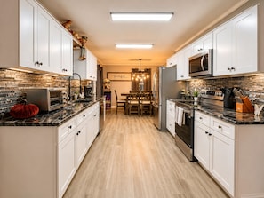 Una cocina moderna con armarios blancos, un microondas, un refrigerador y un comedor con una lámpara de araña.