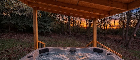 A hot tub under a wooden pergola with a view of a forested area.