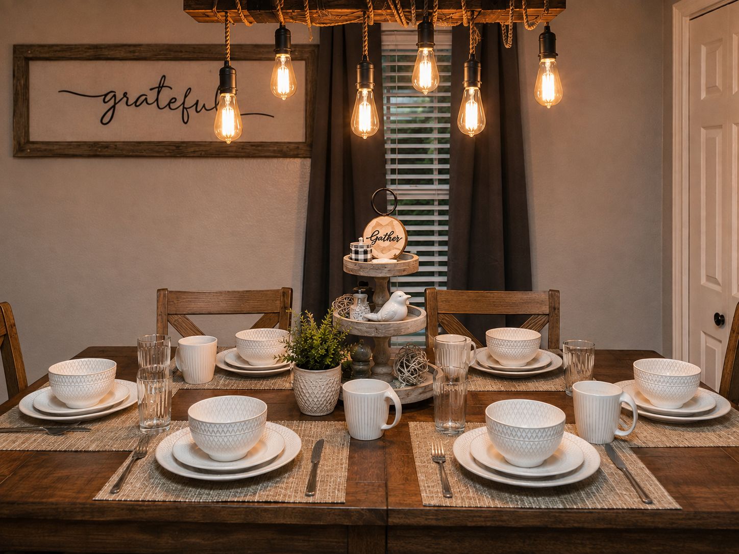 Une table à manger dressée avec des bols, des assiettes et des tasses blancs à motifs, un panneau indiquant « merci » au-dessus et un panneau indiquant « rassemblement » sur un présentoir à plusieurs niveaux.